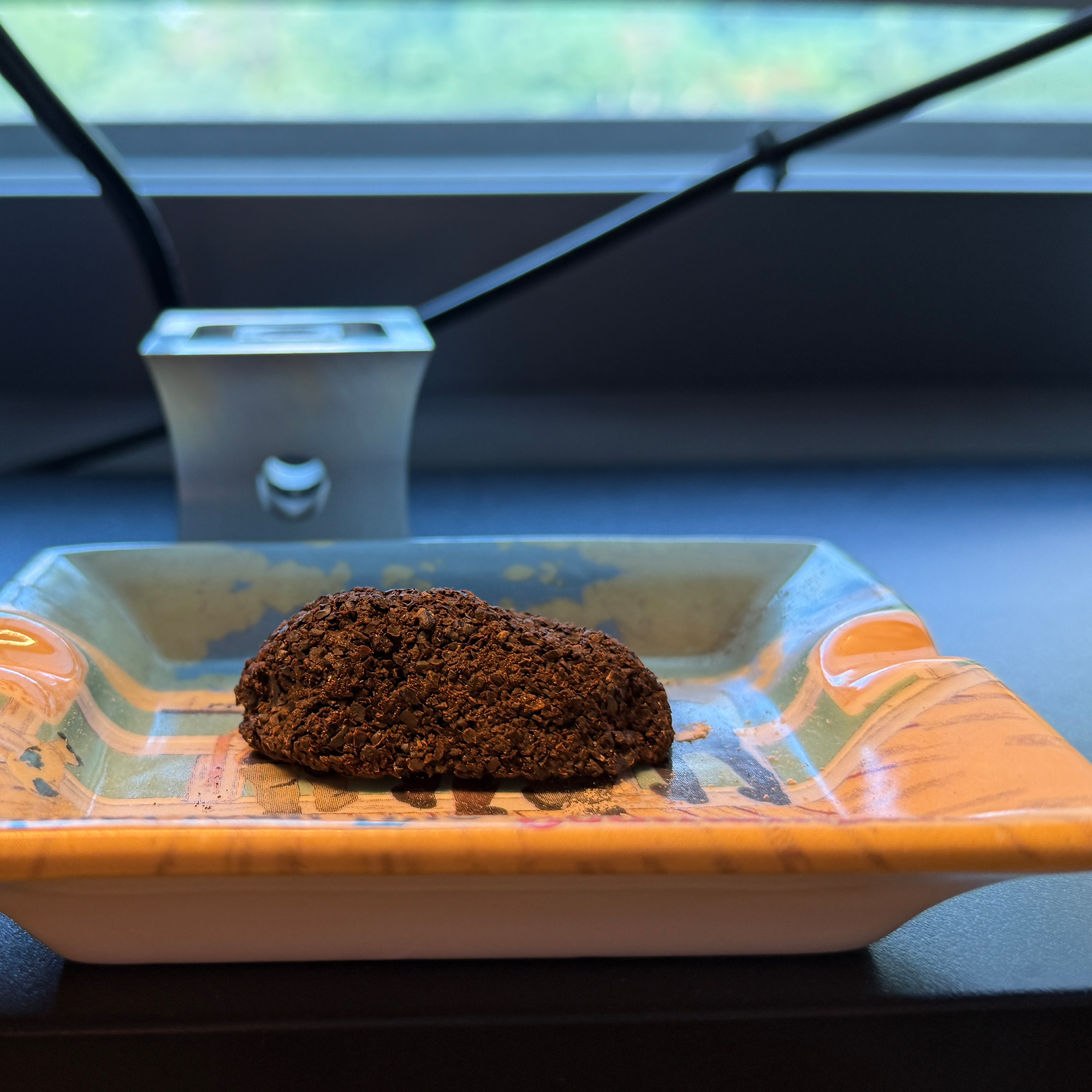 Close-up of a mound of ground coffee on a decorative rectangular glass dish on a dark surface near a window.