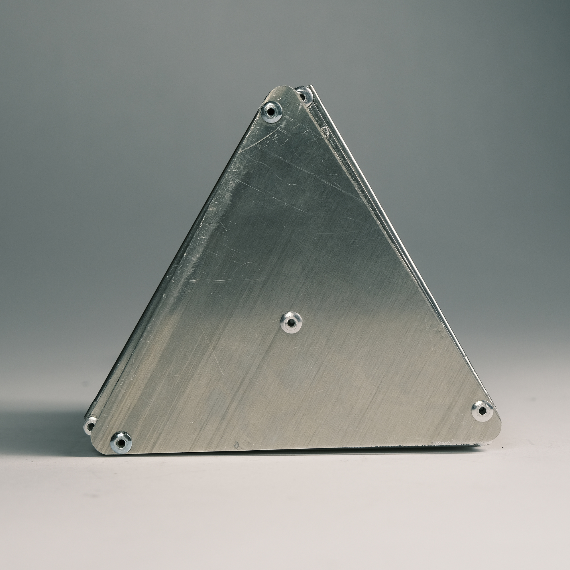Close-up of a triangular metal object with visible screws on a neutral background.