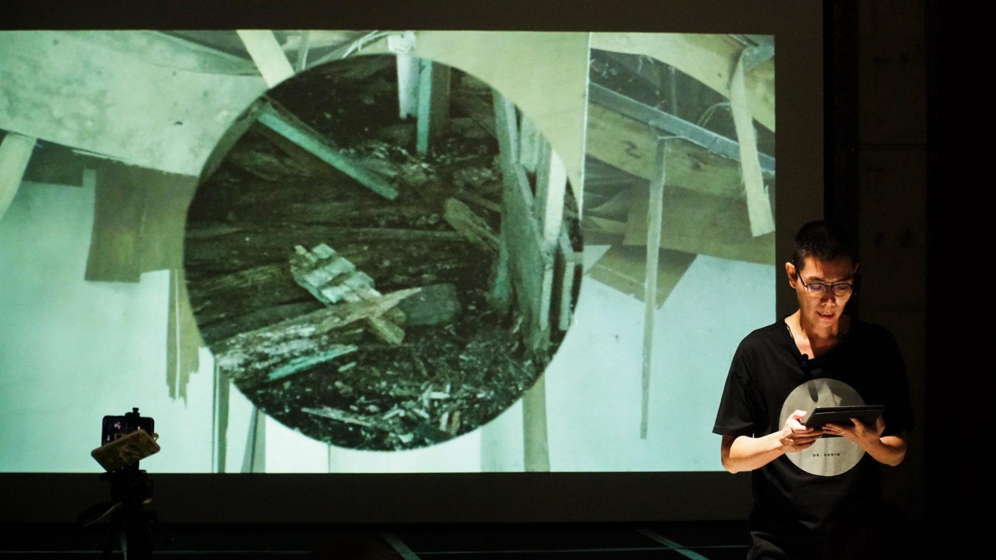 Boedi reading from a tablet in front of a projected image