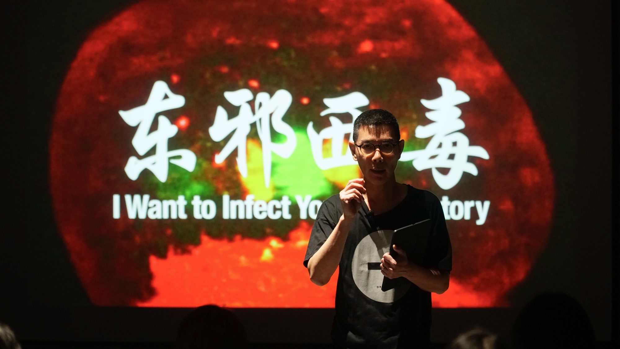 Boedi speaking in front of the projected title 东邪西毒 I Want to Infect You With History