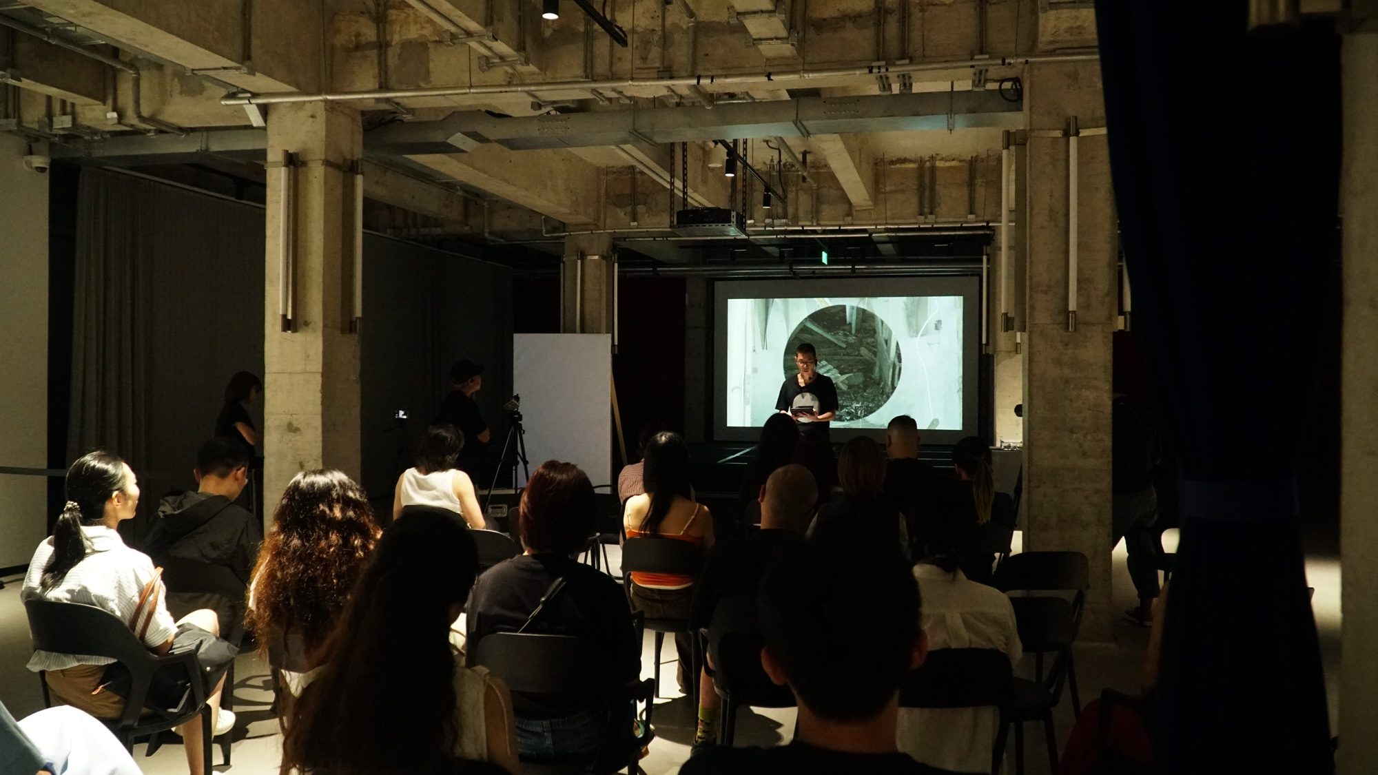 Audience seated in a dim room facing a projection