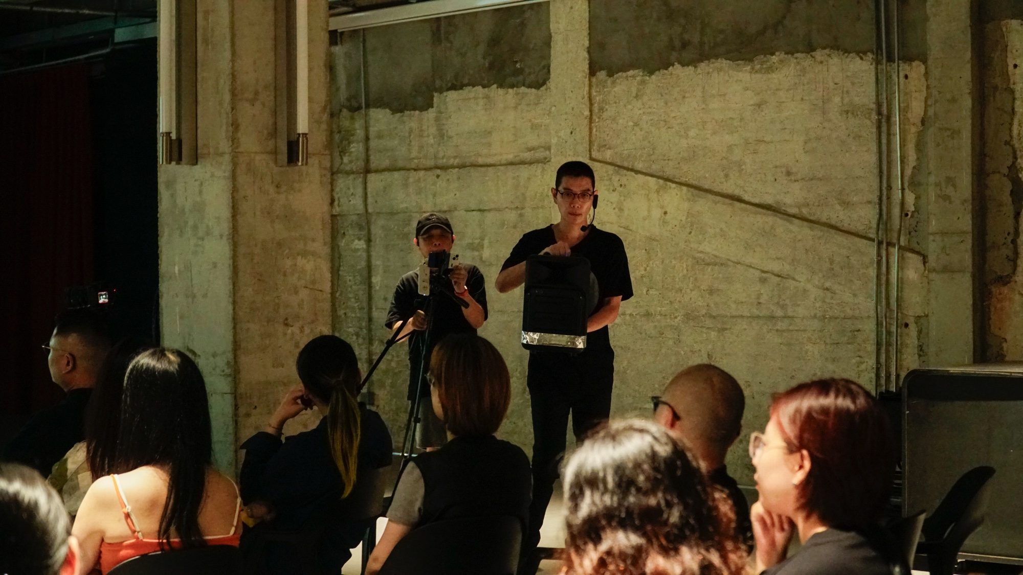 Boedi speaking to the audience beside a concrete wall