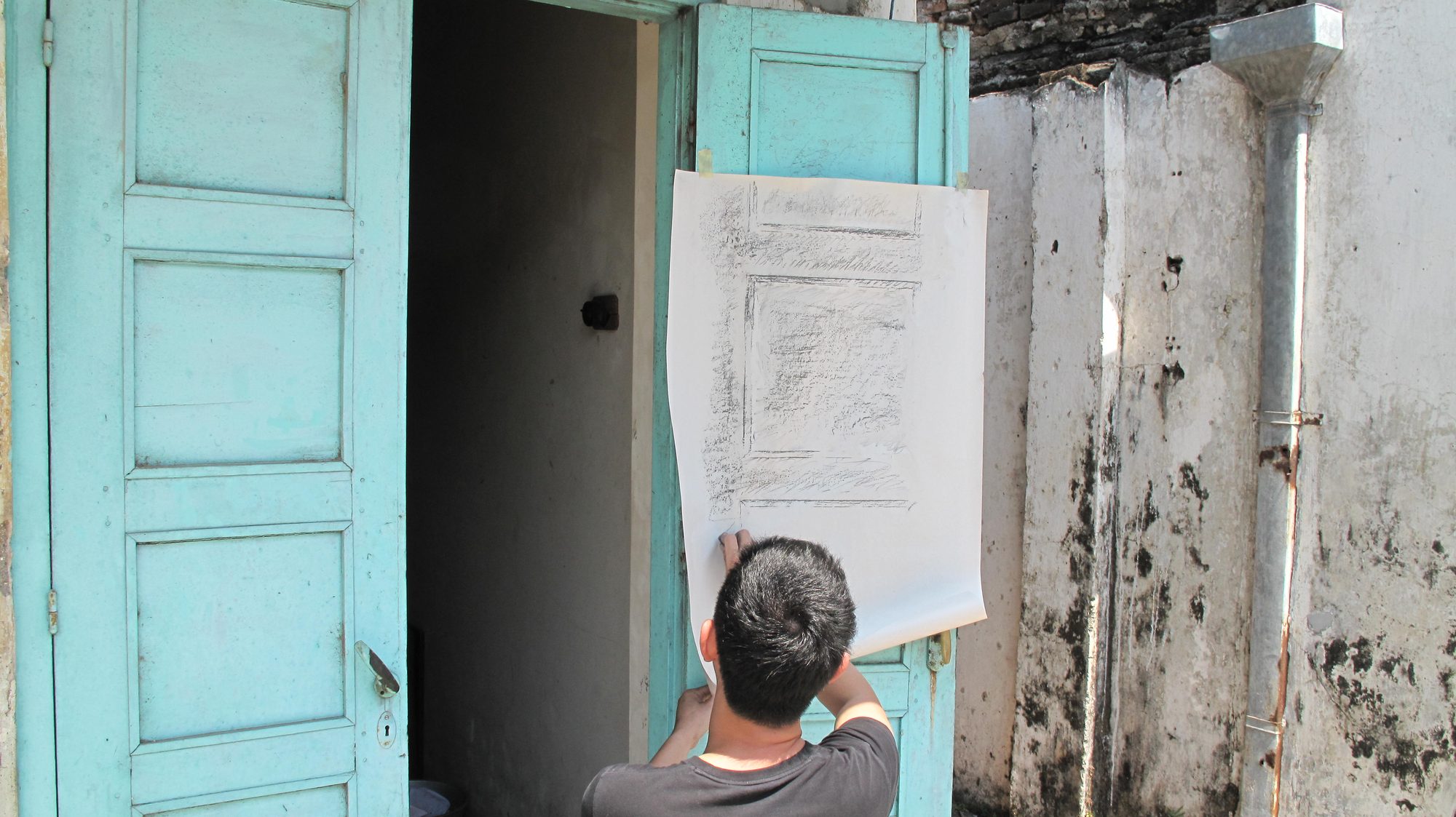 Paper held against a pale blue door for a frottage