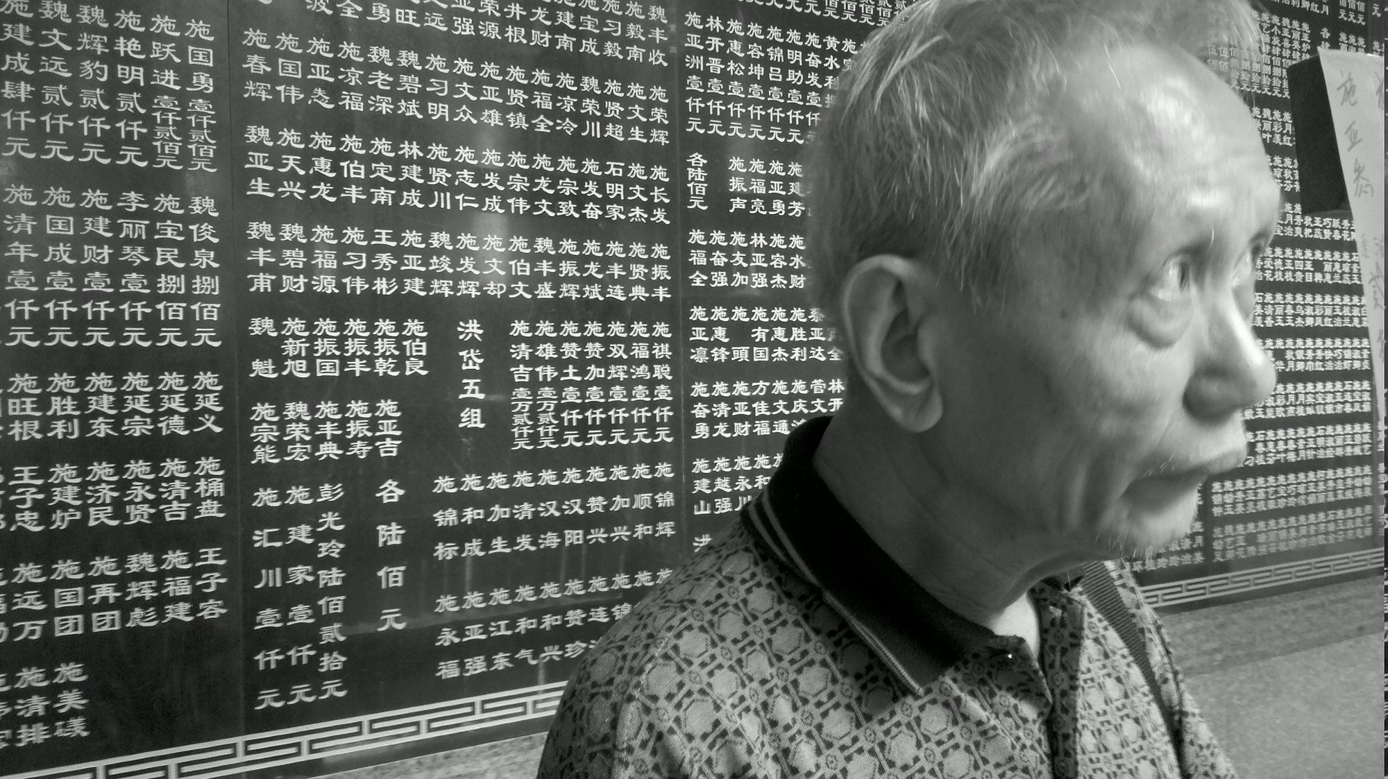 An older man in front of a wall of carved names