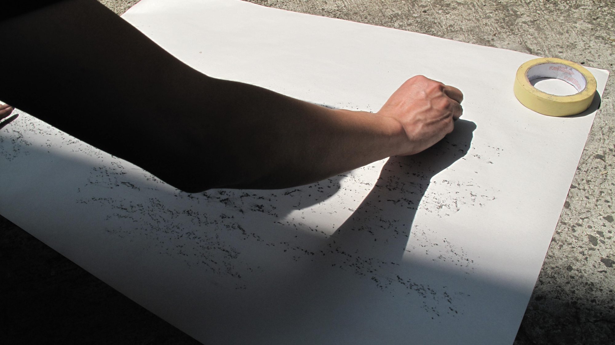 A hand rubbing graphite across paper taped to the ground