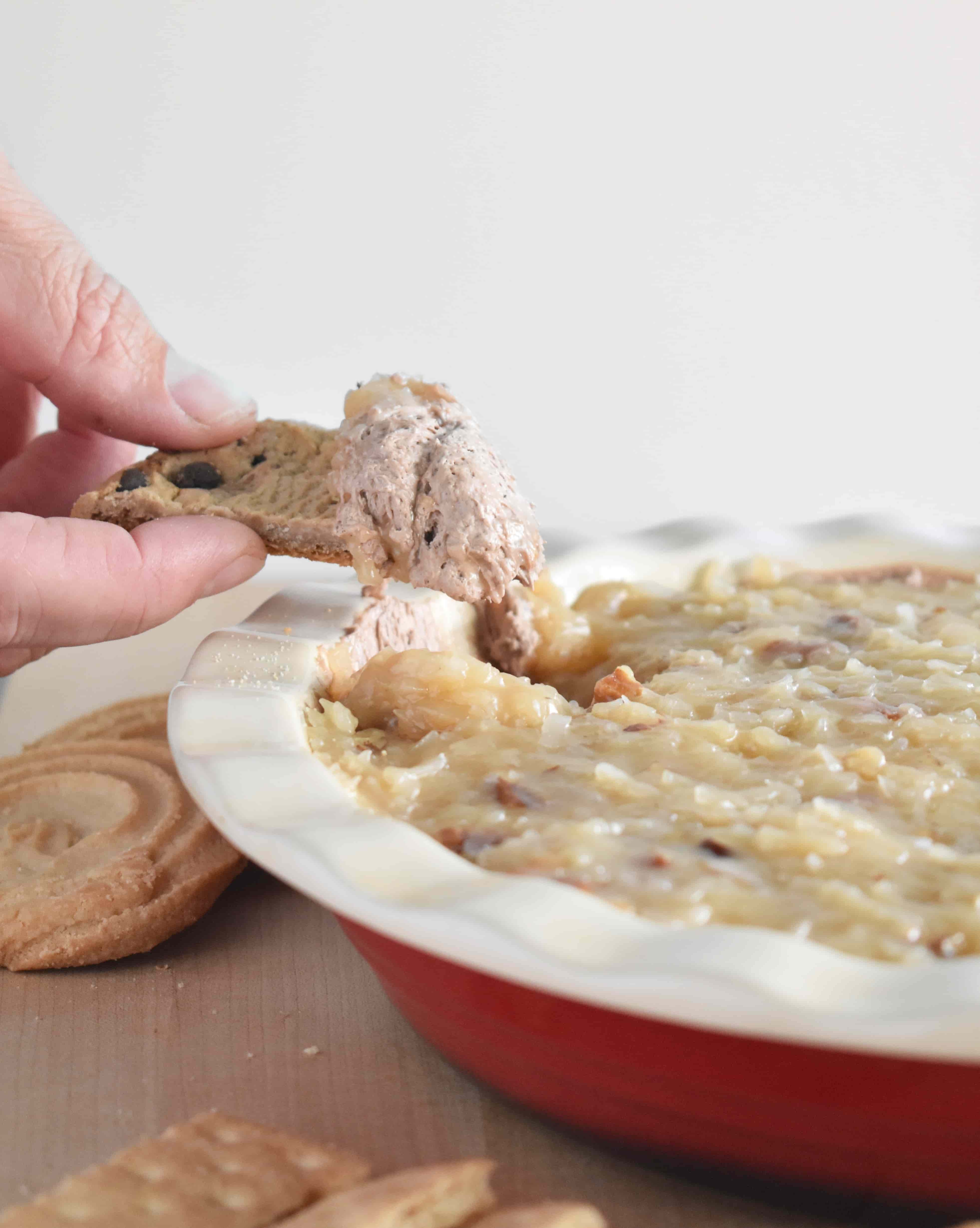 Chocolate chip cookie scooping up German Chocolate Dip, showing the creamy chocolate layer and gooey coconut pecan topping