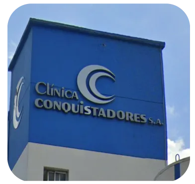 Blue and white building facade with the sign 'Clínica Conquistadores S.A.' under a clear sky.