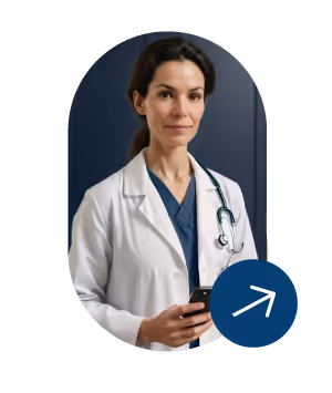 Female doctor in white coat and blue scrubs holding a phone with a stethoscope around her neck.