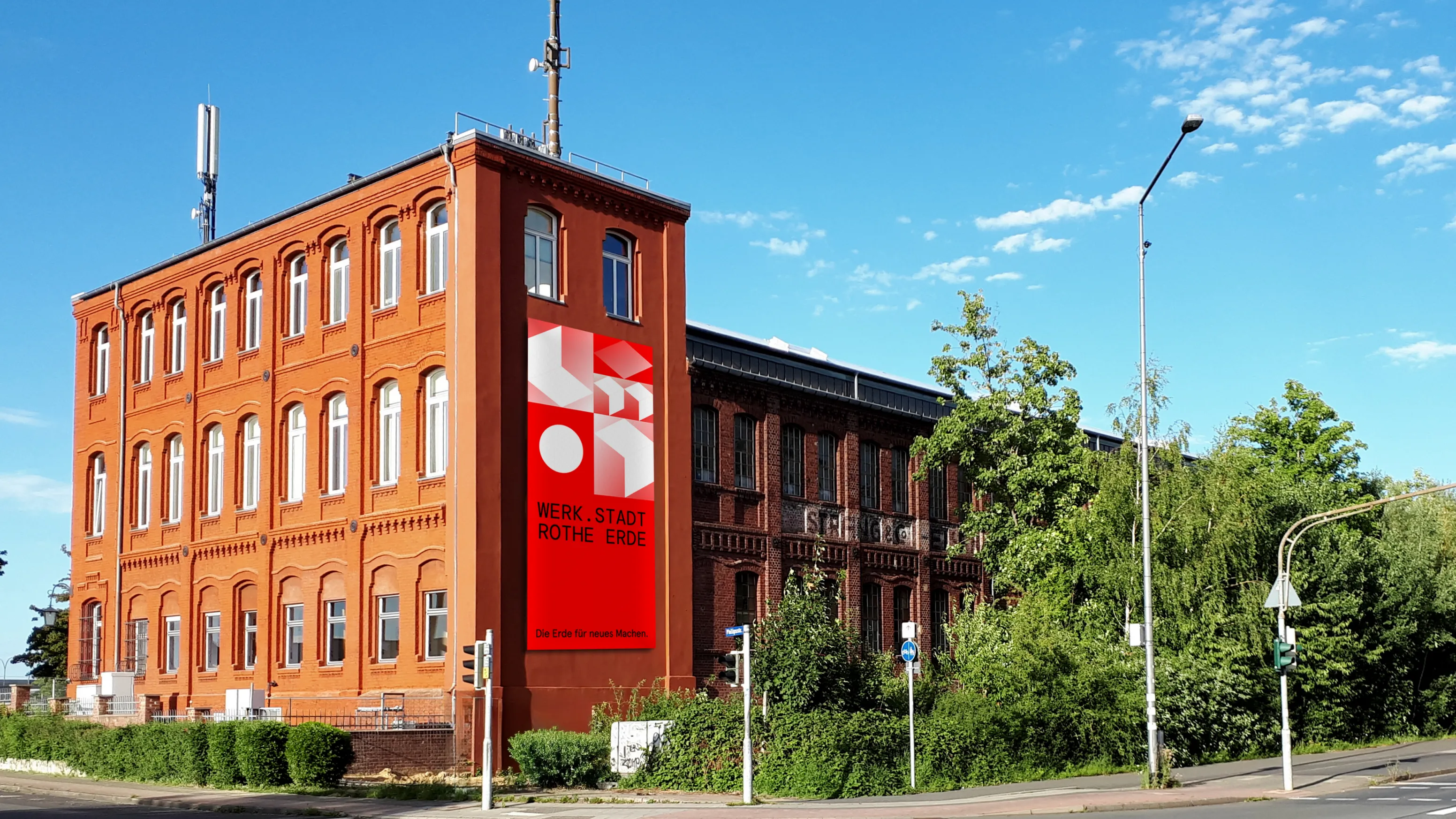 Außenaufnahme der Stranghalle in Aachen mit einem großen vertikalen Banner der WERK.STADT Rothe Erde Identität an der Fassade.