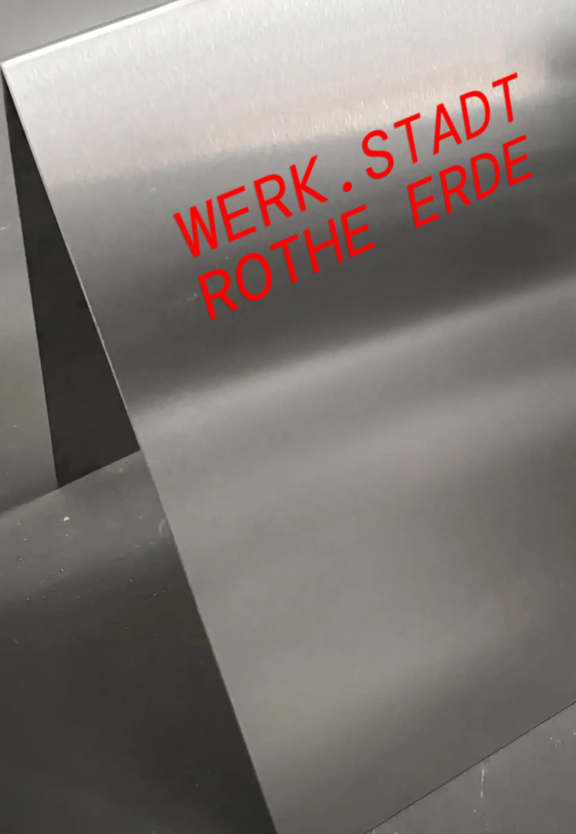 Kundenstopper aus gebürstetem Metall mit rotem Aufdruck „WERK.STADT ROTHE ERDE“.