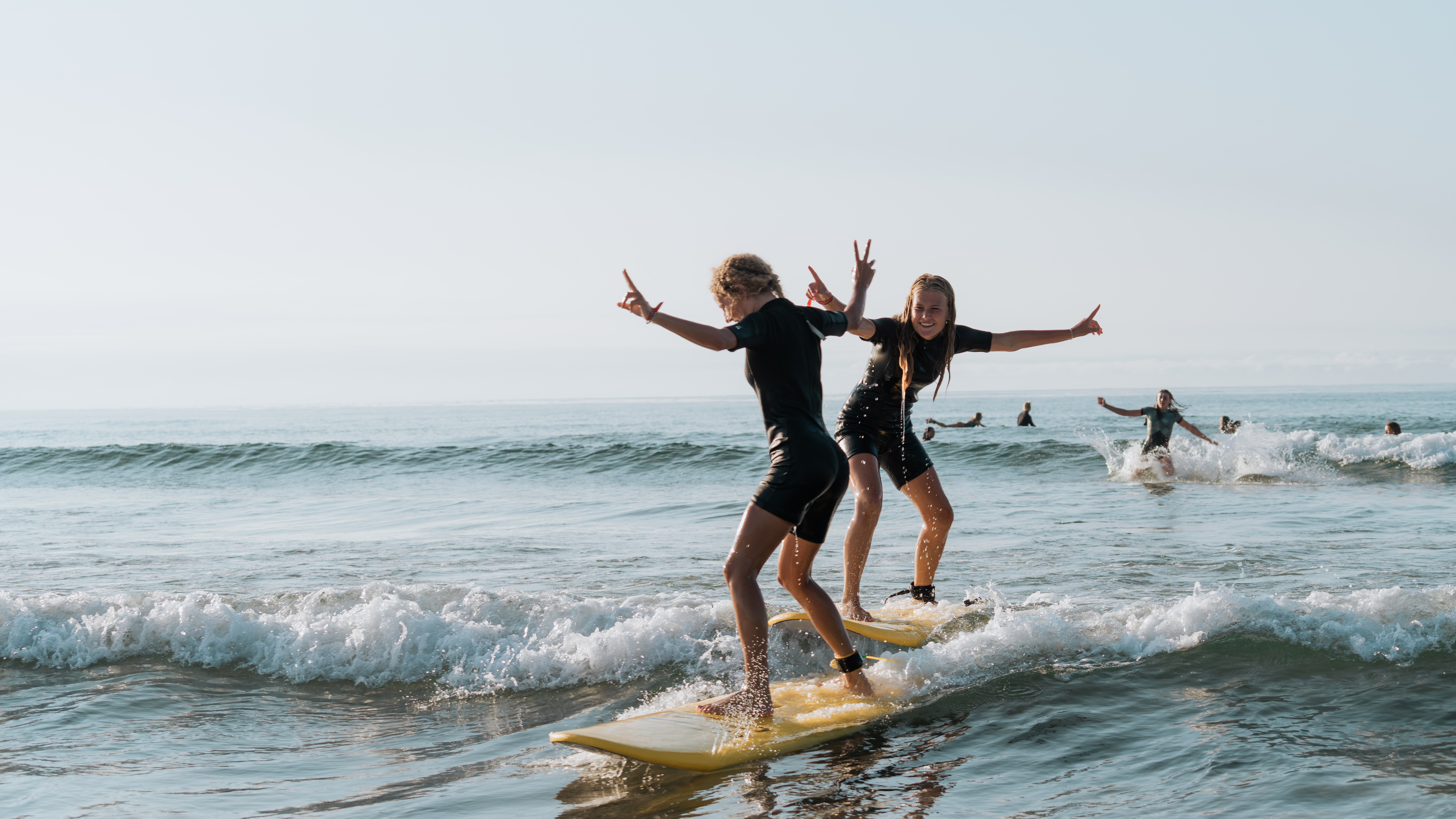 Le Pin Sec surfkamp - twee meisjes surfen met peace teken