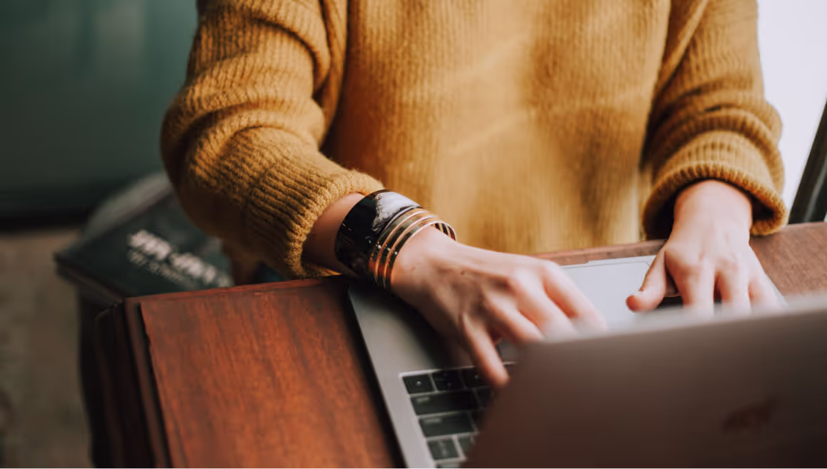 Woman in mustard yellow sweater types on a laptop