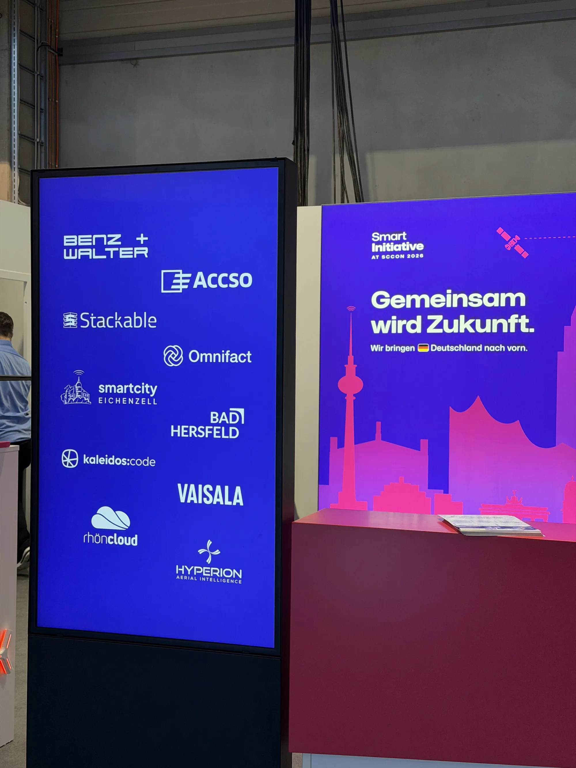 Digitale Stele mit allen Partnerlogos neben der Leuchtwand mit dem Claim Gemeinsam wird Zukunft
