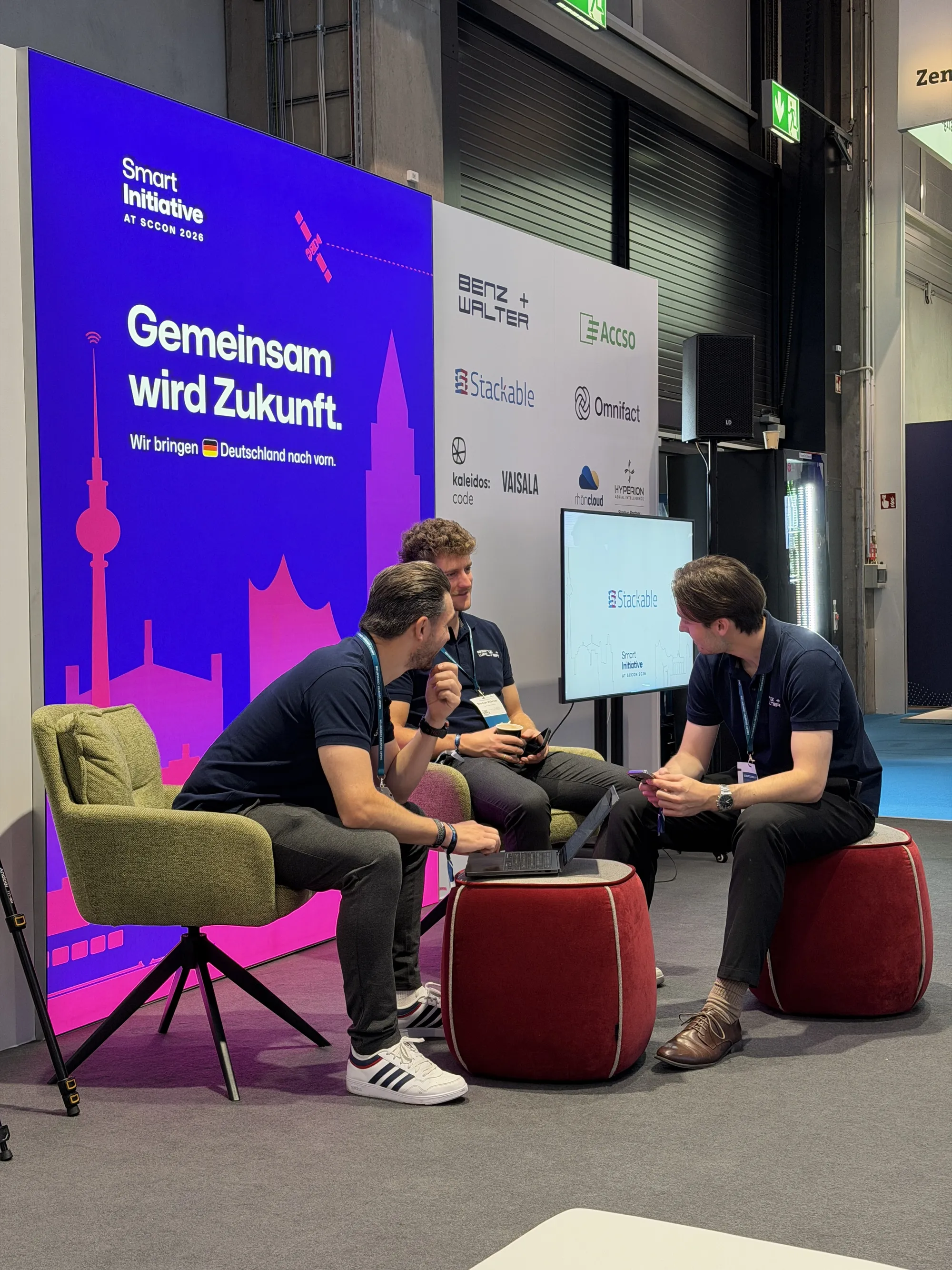 Gespräch in der Lounge des Smart-Initiative-Stands vor der Leuchtwand und der Partnerwand