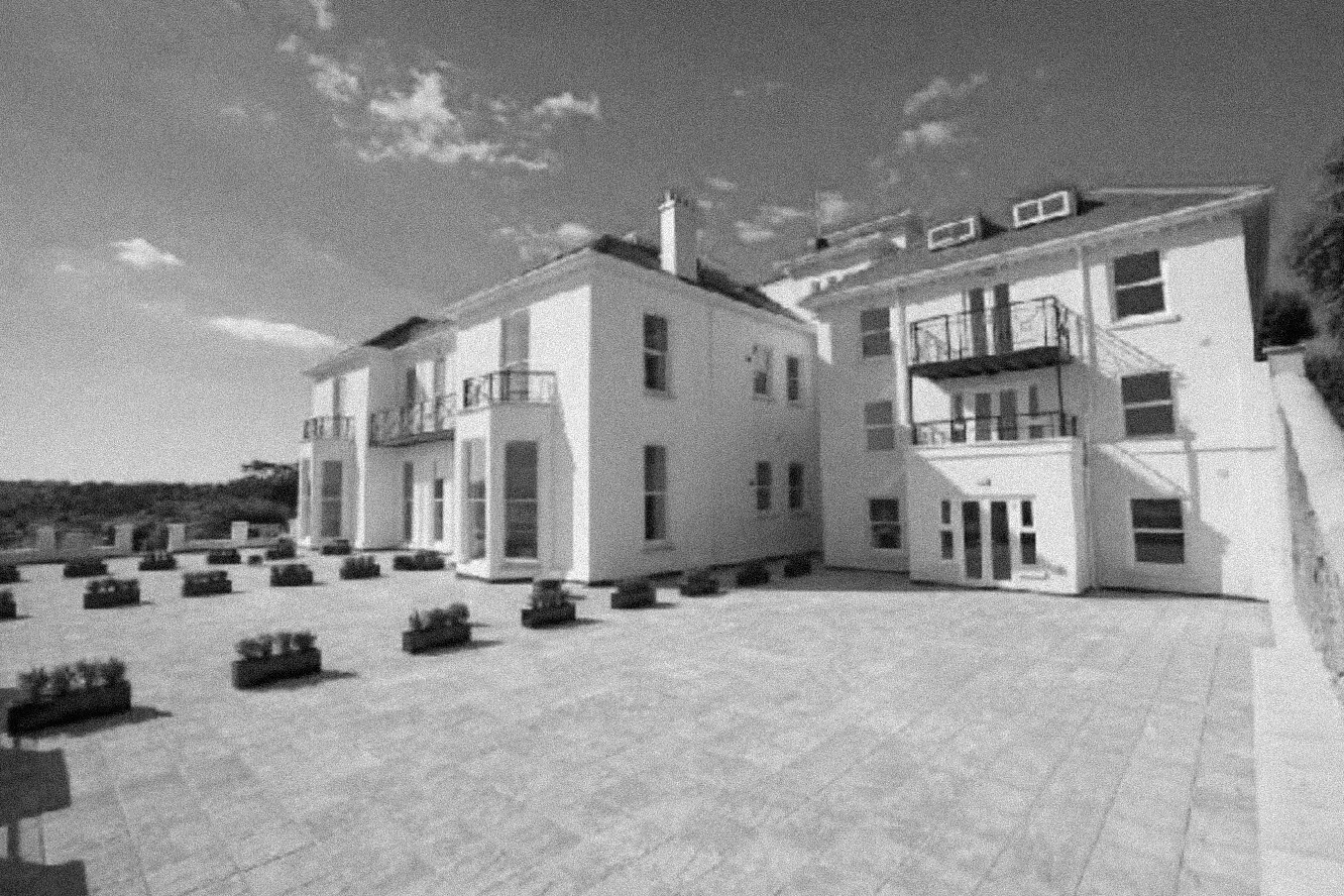 Large white multi-story house with balconies and a spacious tiled patio area featuring multiple planter boxes.