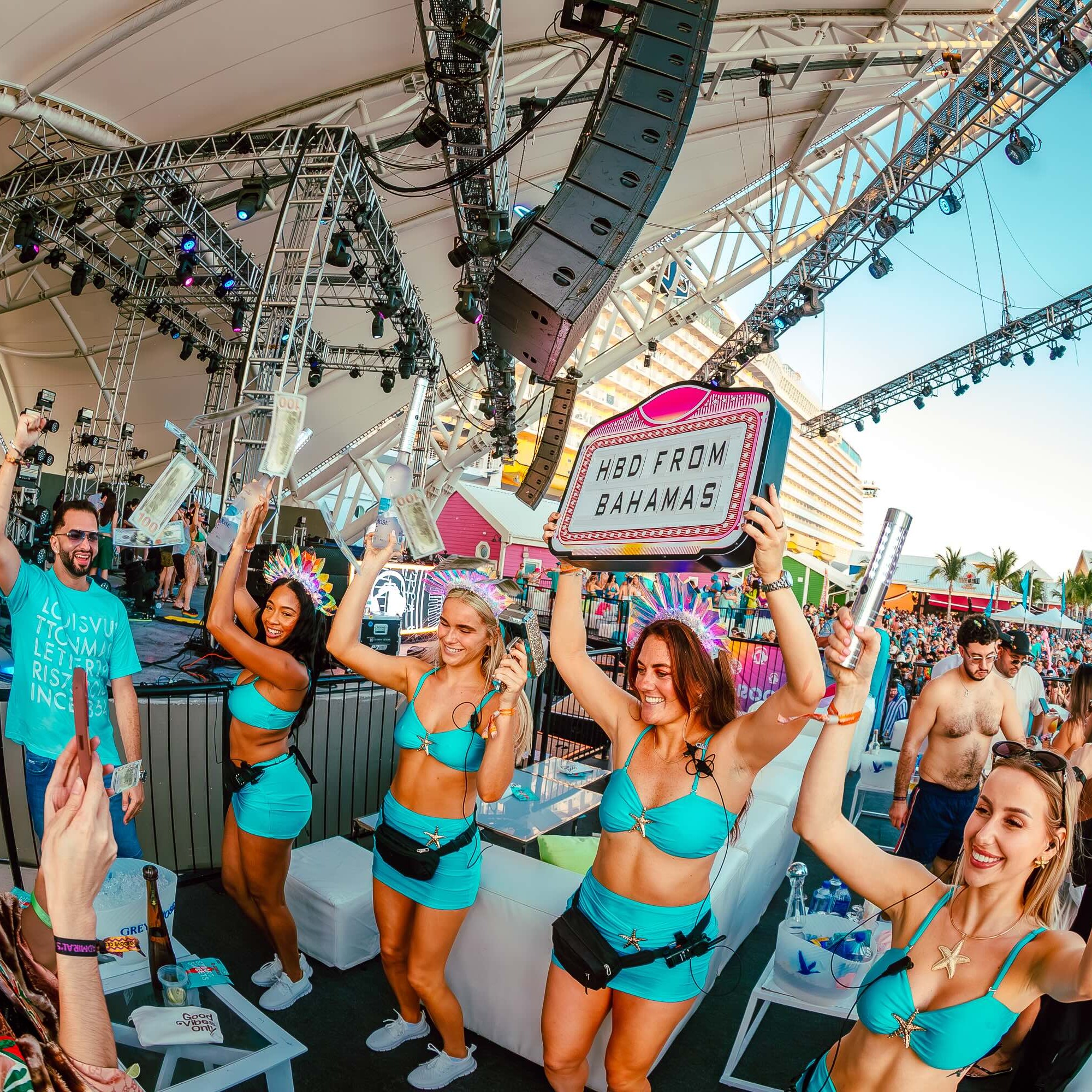 Guests cheer beside an outdoor stage during a Groove Cruise VIP bottle service celebration.