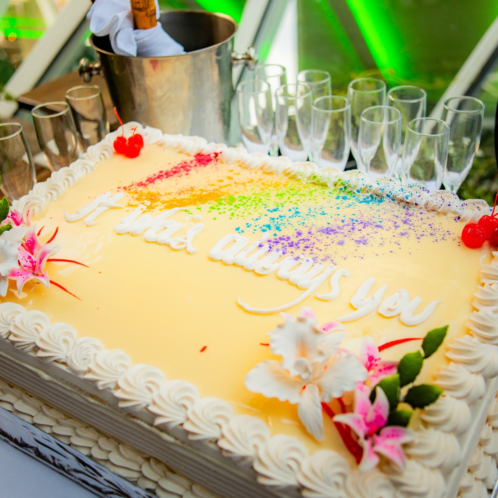  Anniversary celebration cake with rainbow decorations beside champagne glasses onboard a Miami rave cruise.
