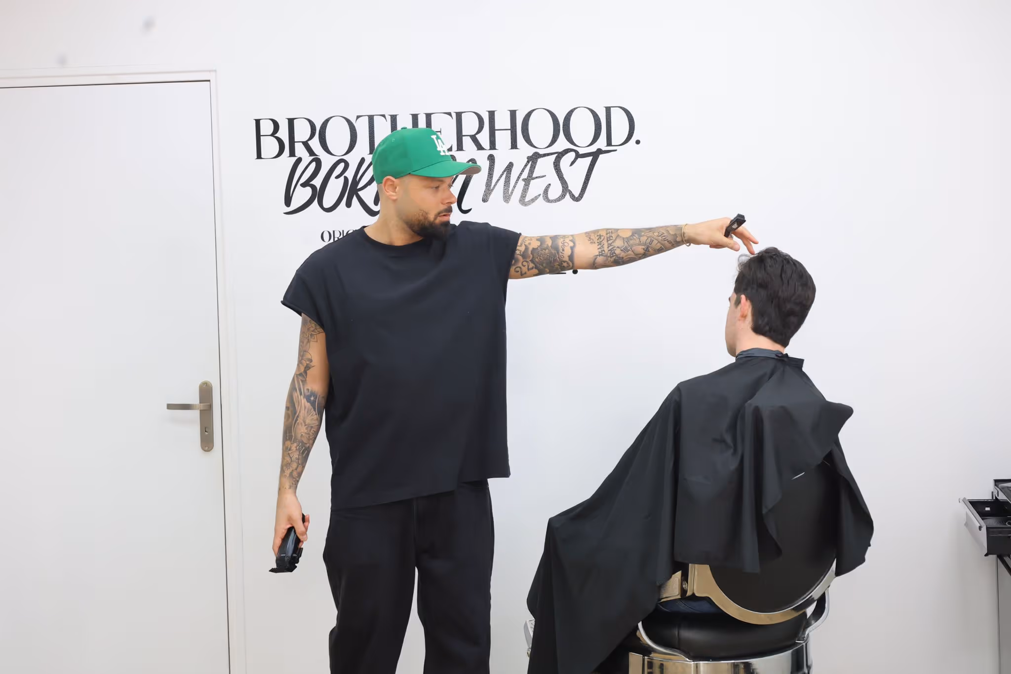 Baki expert barbier en t-shirt noir et casquette verte coupe les cheveux d'un client en salon moderne.