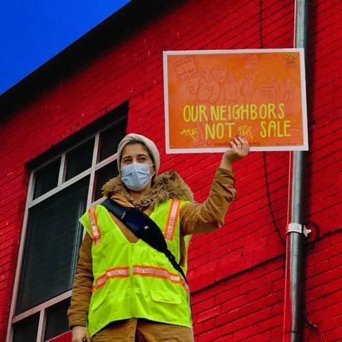 person holds sign in front of red building