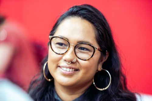 Person wearing glasses and hoop earring smiles in front of red background