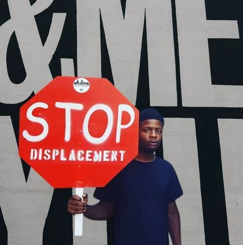Person holds a red sign shaped like stop sign that says STOP Displacement