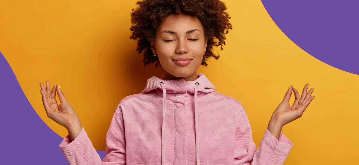 A woman meditating with her hands up and eyes closed, against a purple and yellow Designity background.