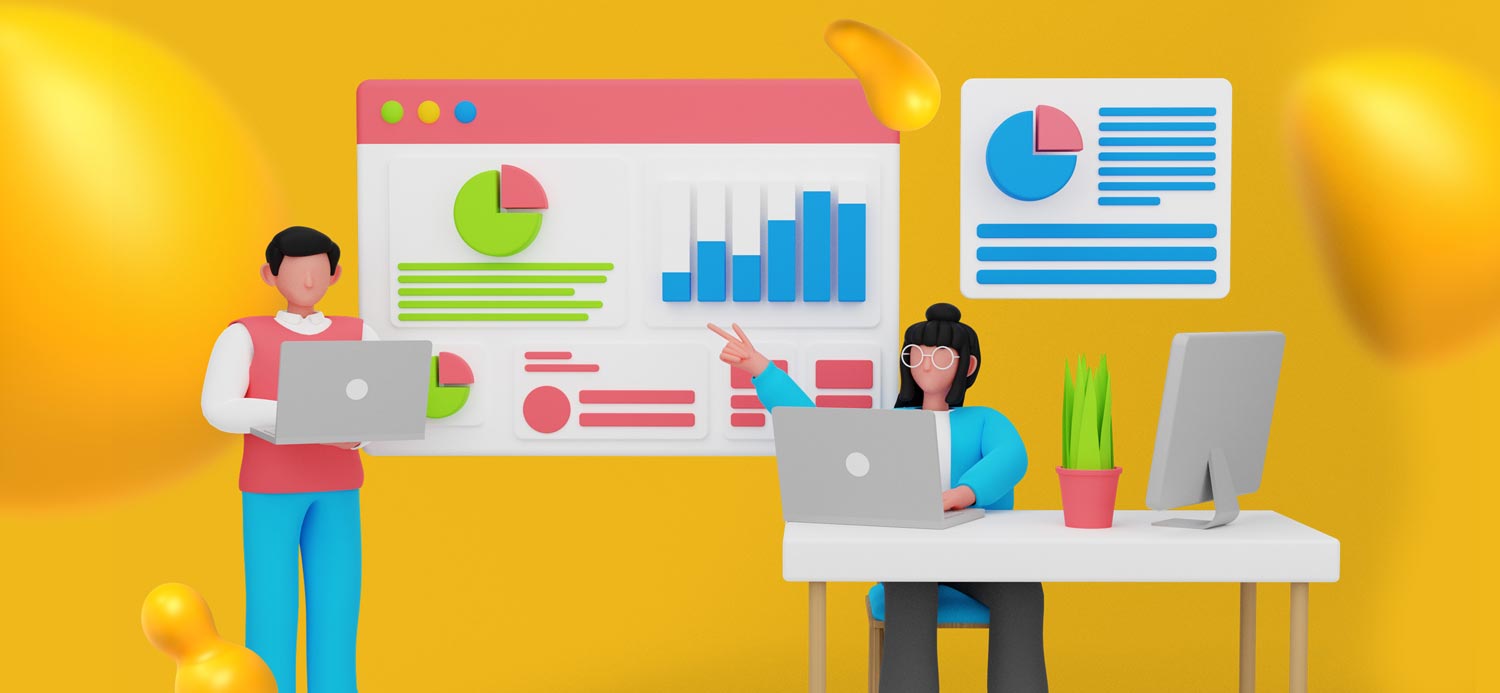 Two people in an office. A woman sits at a desk with her laptop and is pointing at a chart. The man is standing, taking notes on his own laptop.