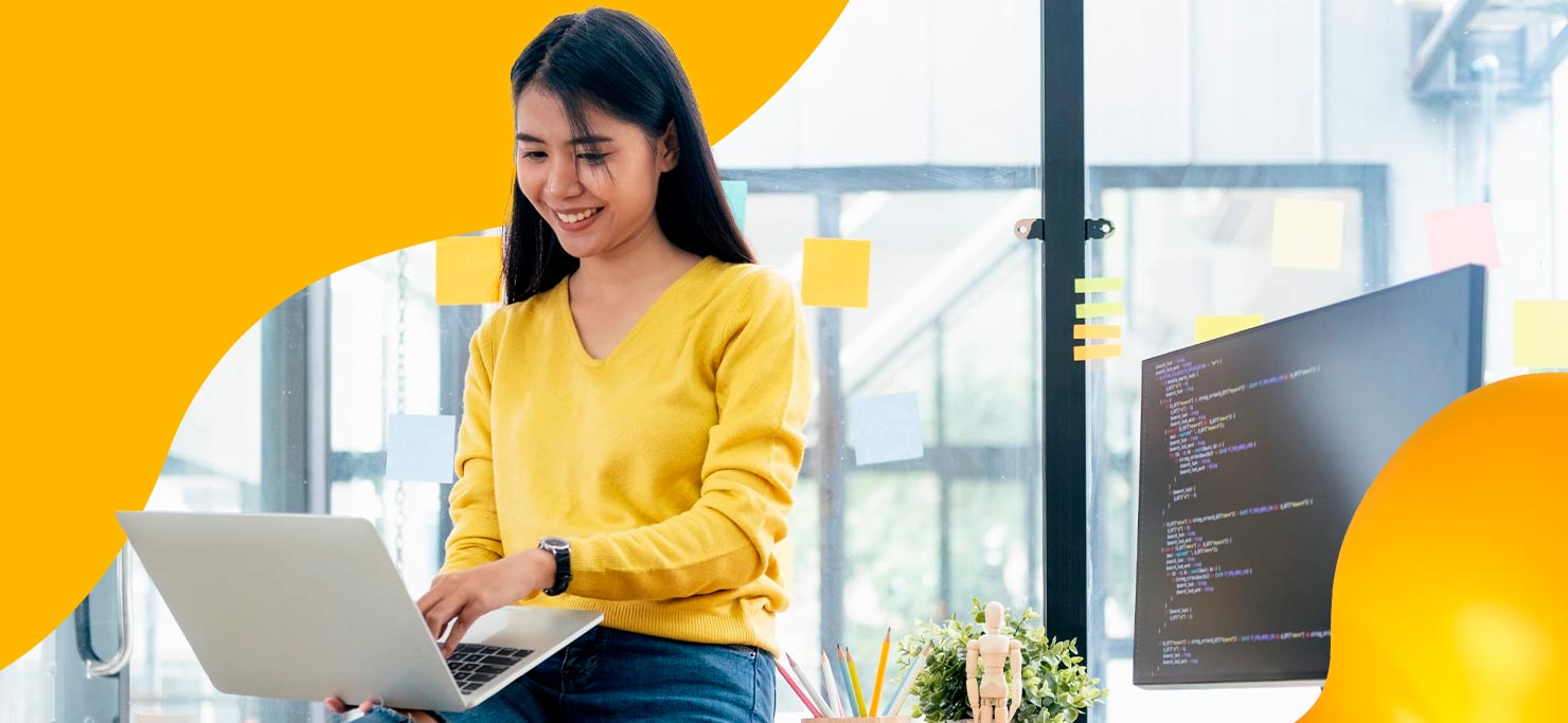 A smiling woman in a yellow shirt works on a laptop. She is set against a yellow blob Designity background.