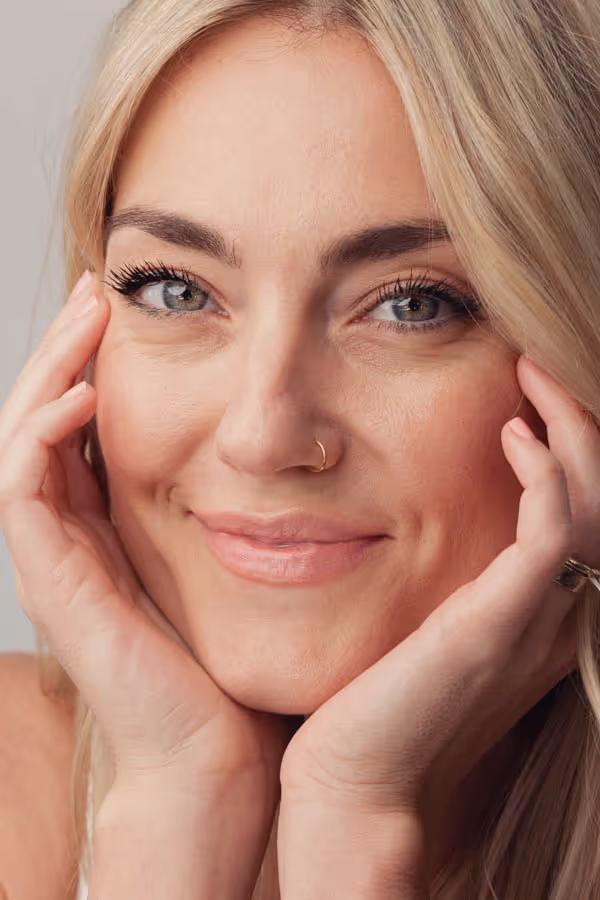 Headshot of a blond woman with her hands framing her face