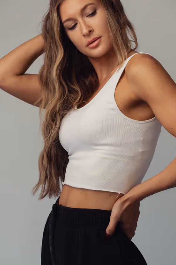 Woman standing with eyes downcast, posing with one hand on her hip and the other in her hair