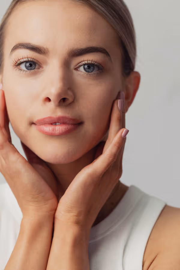 Headshot of a woman with clear skin, and her hands framing her lower face