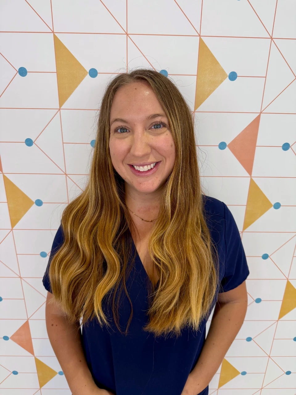 Poppy Kids office coordinator Emily in her uniform in front of a triangular background.