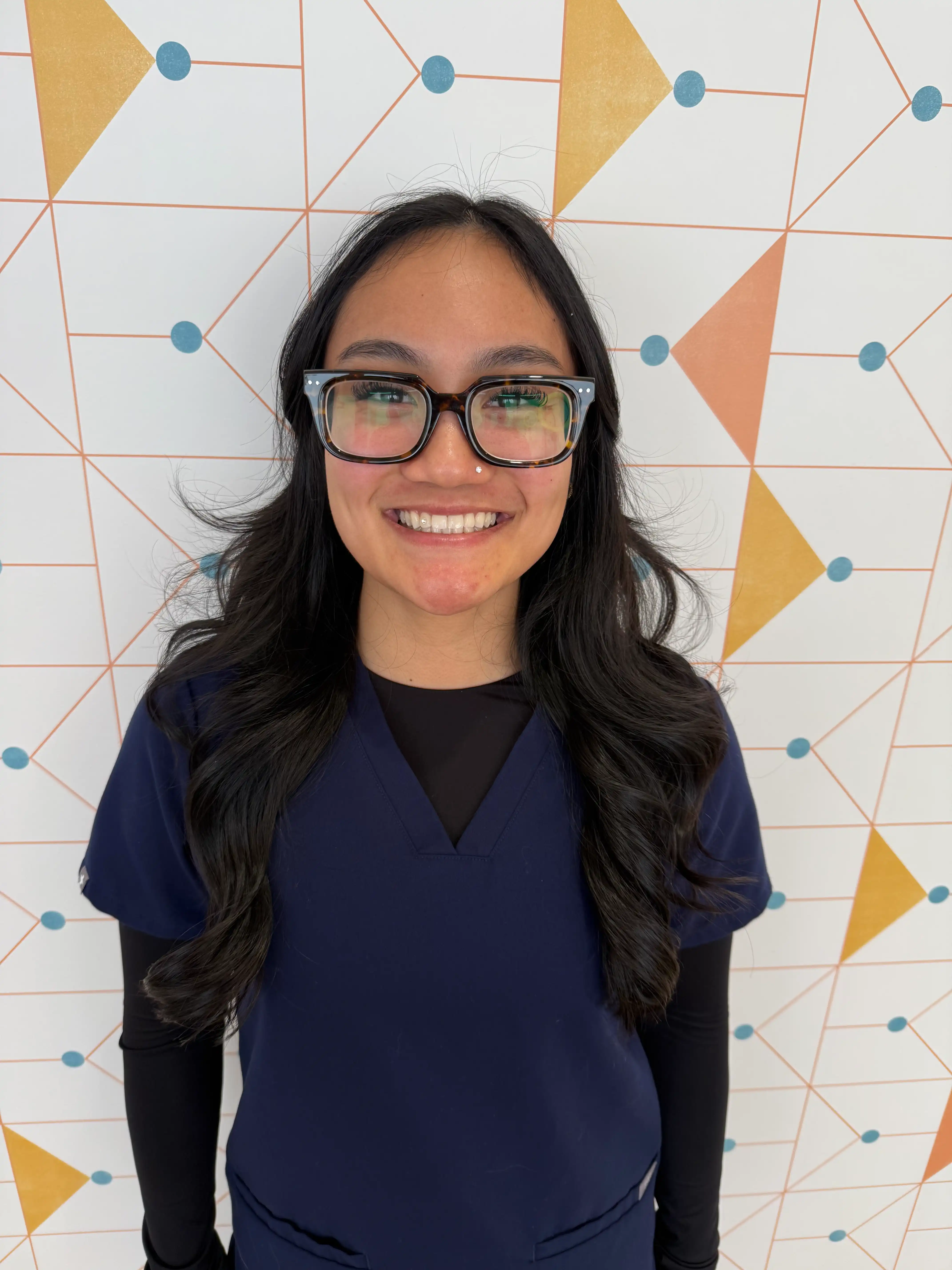 Poppy Kids office coordinator Neah stands leaning against a patterned wall.