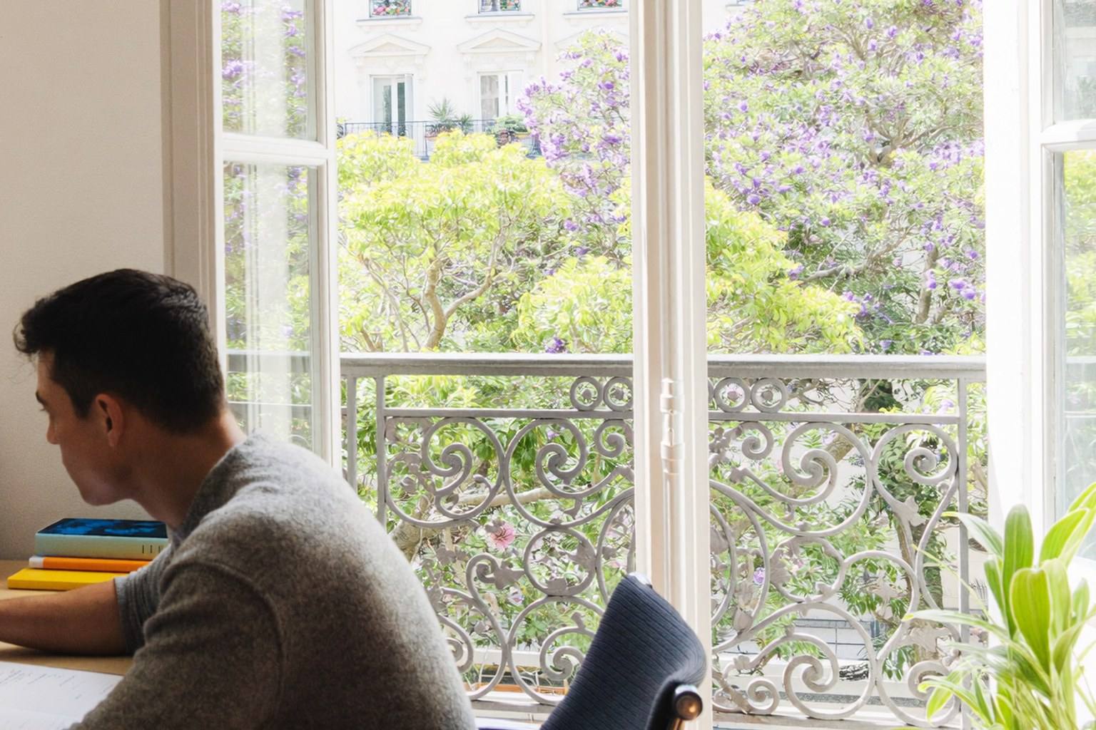 Contractor working at a desk by open French doors with an iron balcony and flowering trees outside
