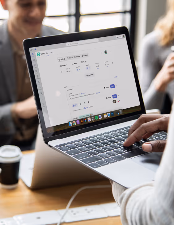 Person using a laptop showing Seatti employee scheduling software with coworkers in background.