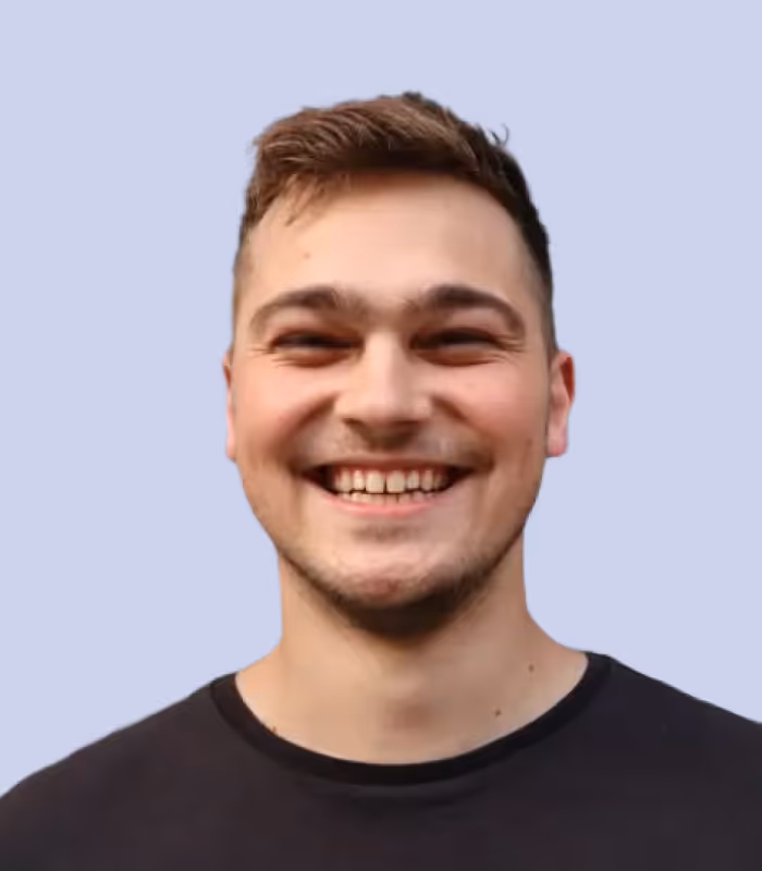 Junger Mann mit kurzem Haar lacht freundlich vor hellem Hintergrund.