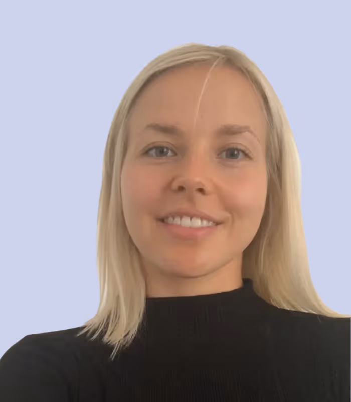 Porträt einer lächelnden jungen Frau mit blonden Haaren und schwarzem Pullover vor hellblauem Hintergrund.