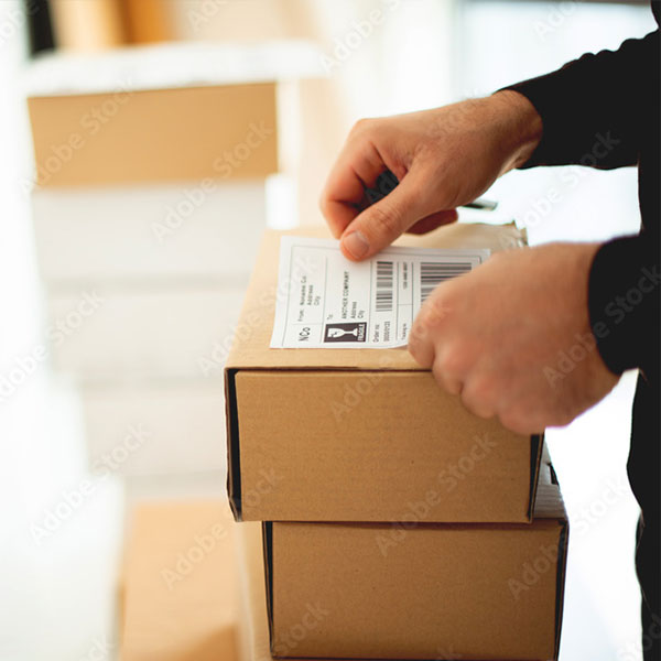 Verkkokauppias valmistelee pakettia lähetystä varten liimaamalla rahtikirjan pahvilaatikon päälle.