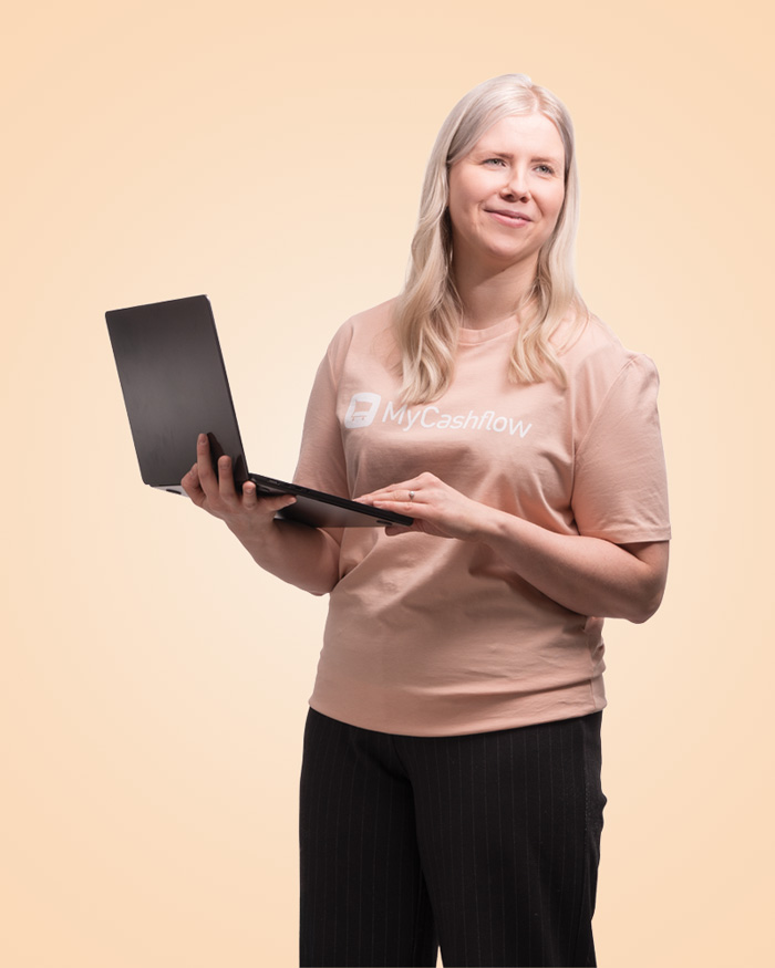 Nainen työskentelee kannettavalla tietokoneella MyCashflow-paita päällä vihreää taustaa vasten.