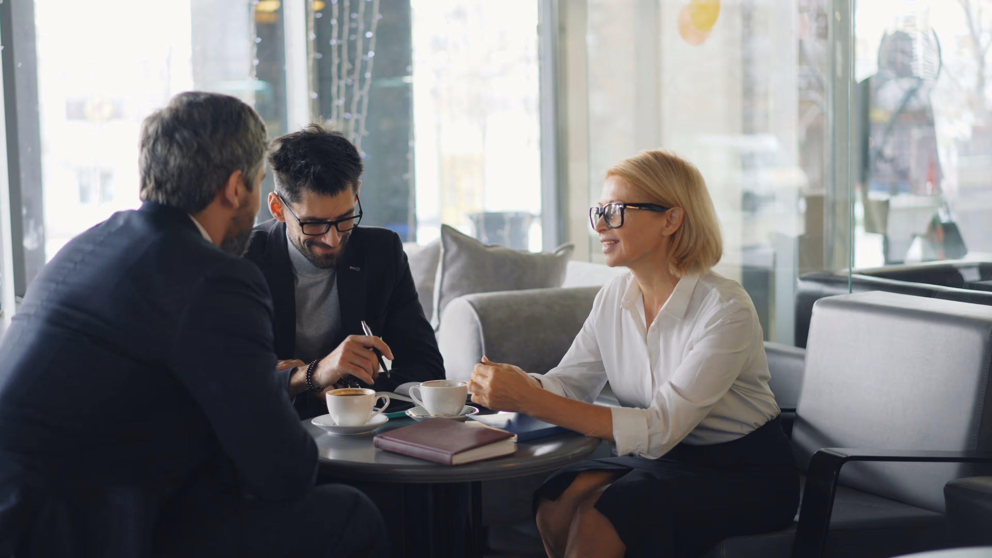 Three professionals sitting around a table in a modern cafe having coffee and discussion.
