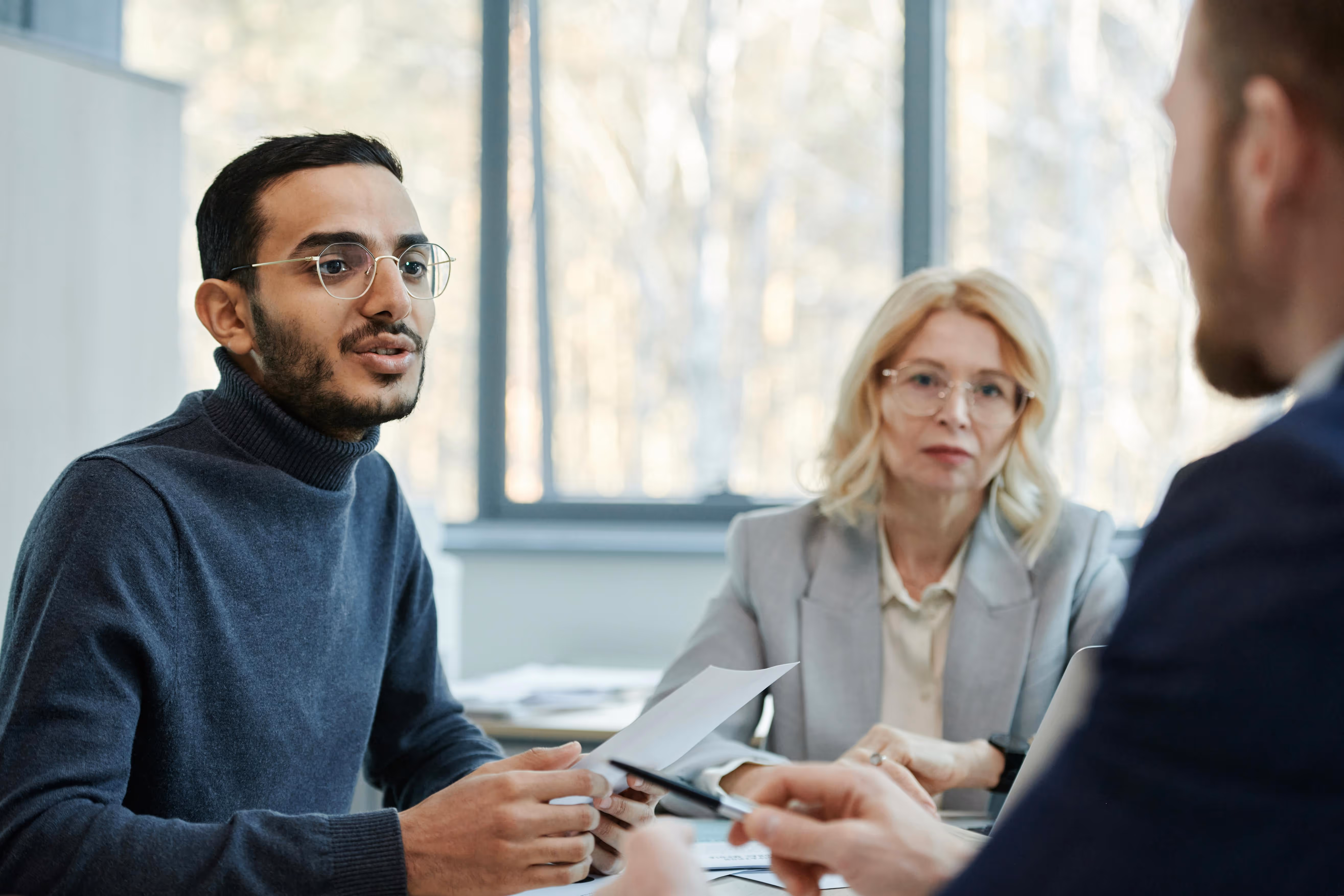 Three diverse professionals having a serious discussion in a bright office with large windows.