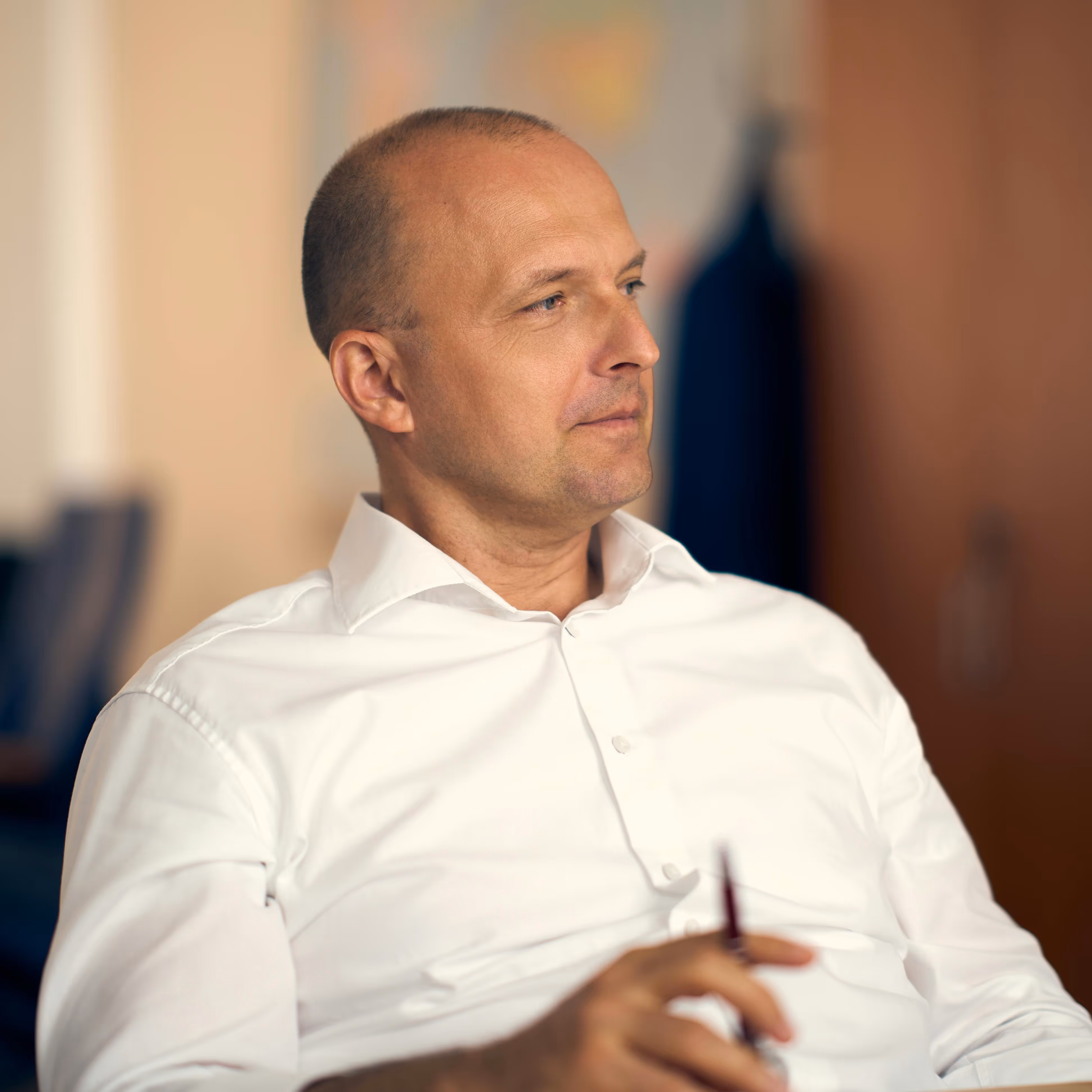Man in a white dress shirt looking thoughtfully to the side while holding a pen.