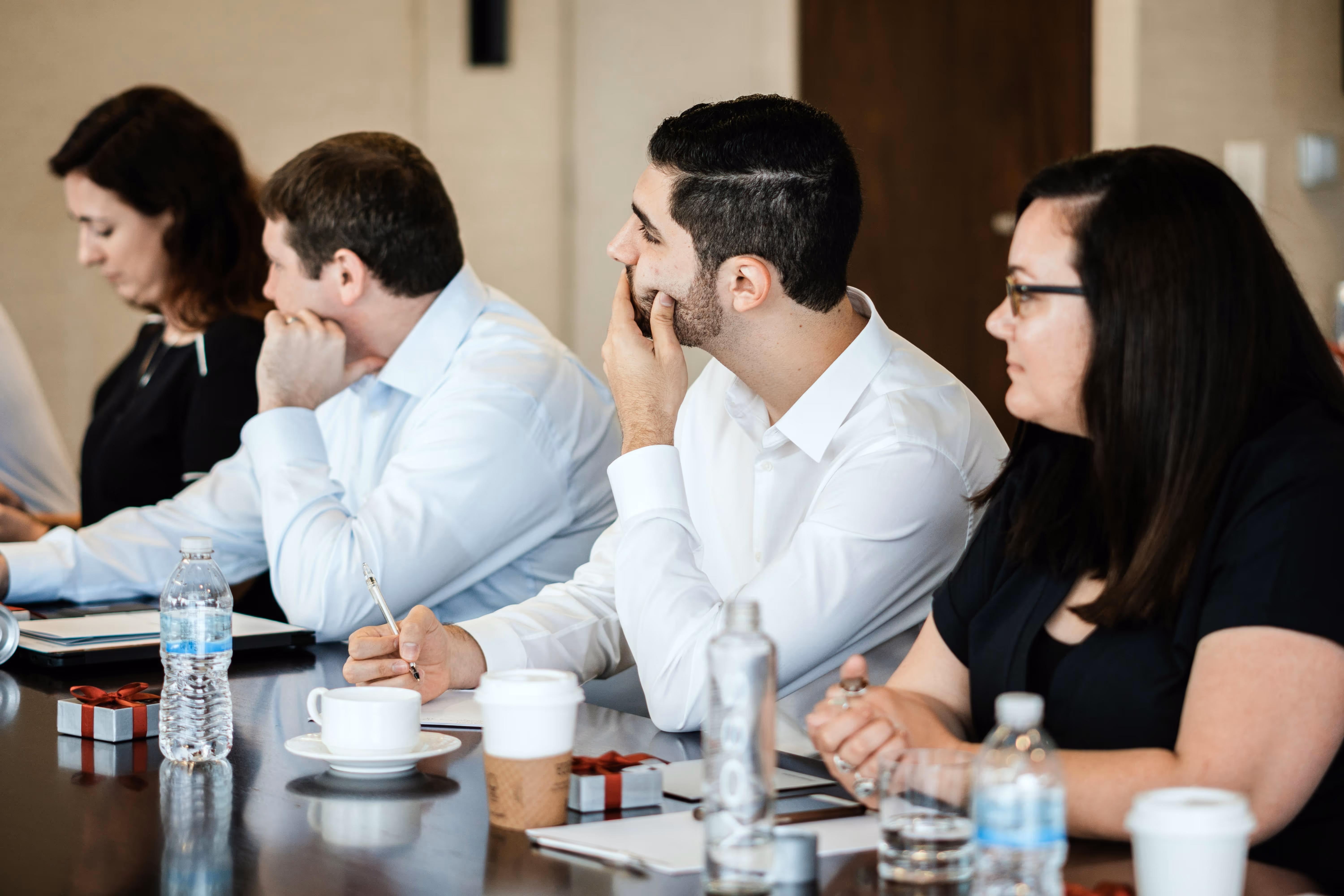 Four professionals seated at a conference table during a meeting, with notebooks, drinks, and water bottles in front of them.