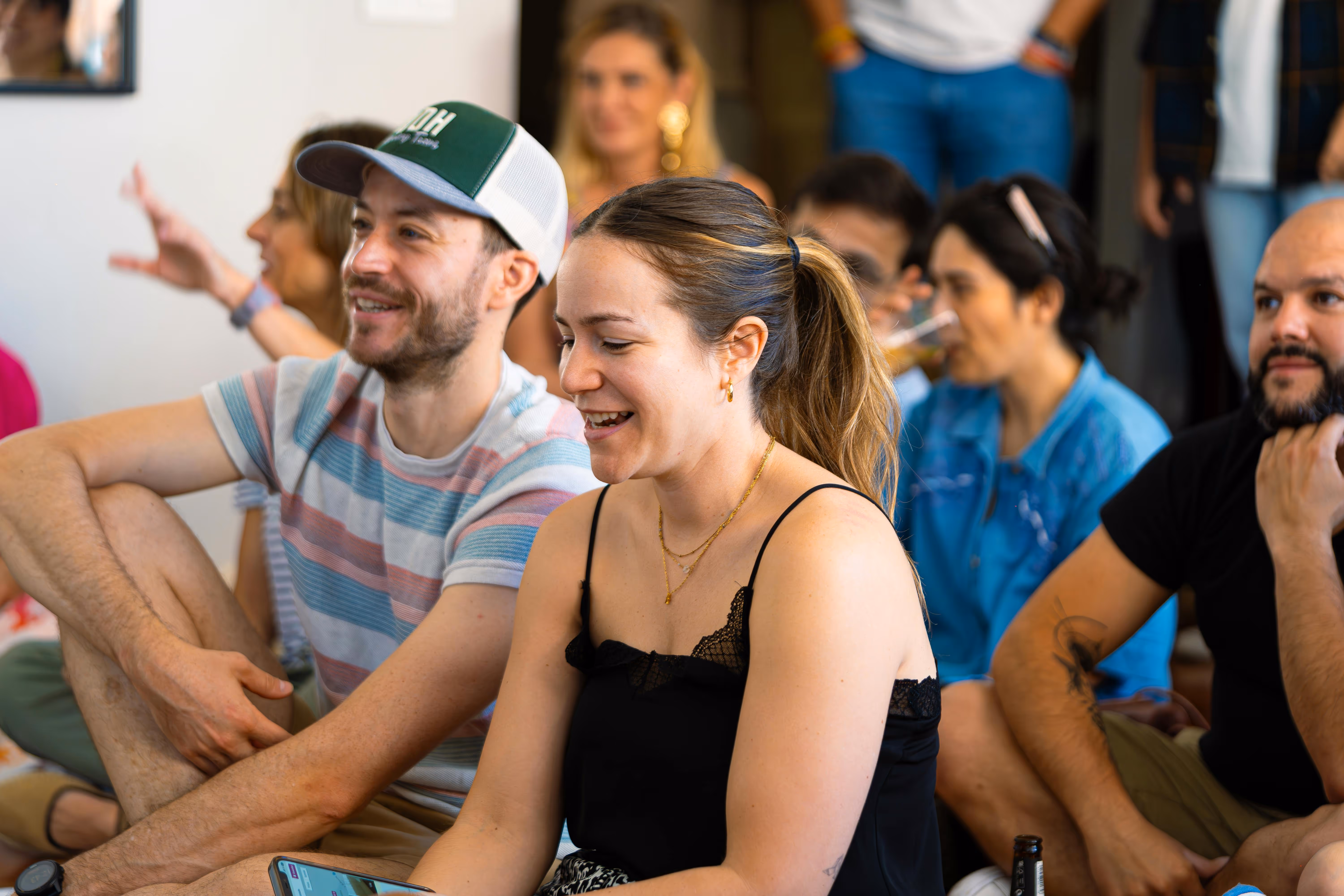 Group of casually dressed people sitting closely indoors, smiling and engaging in conversation.