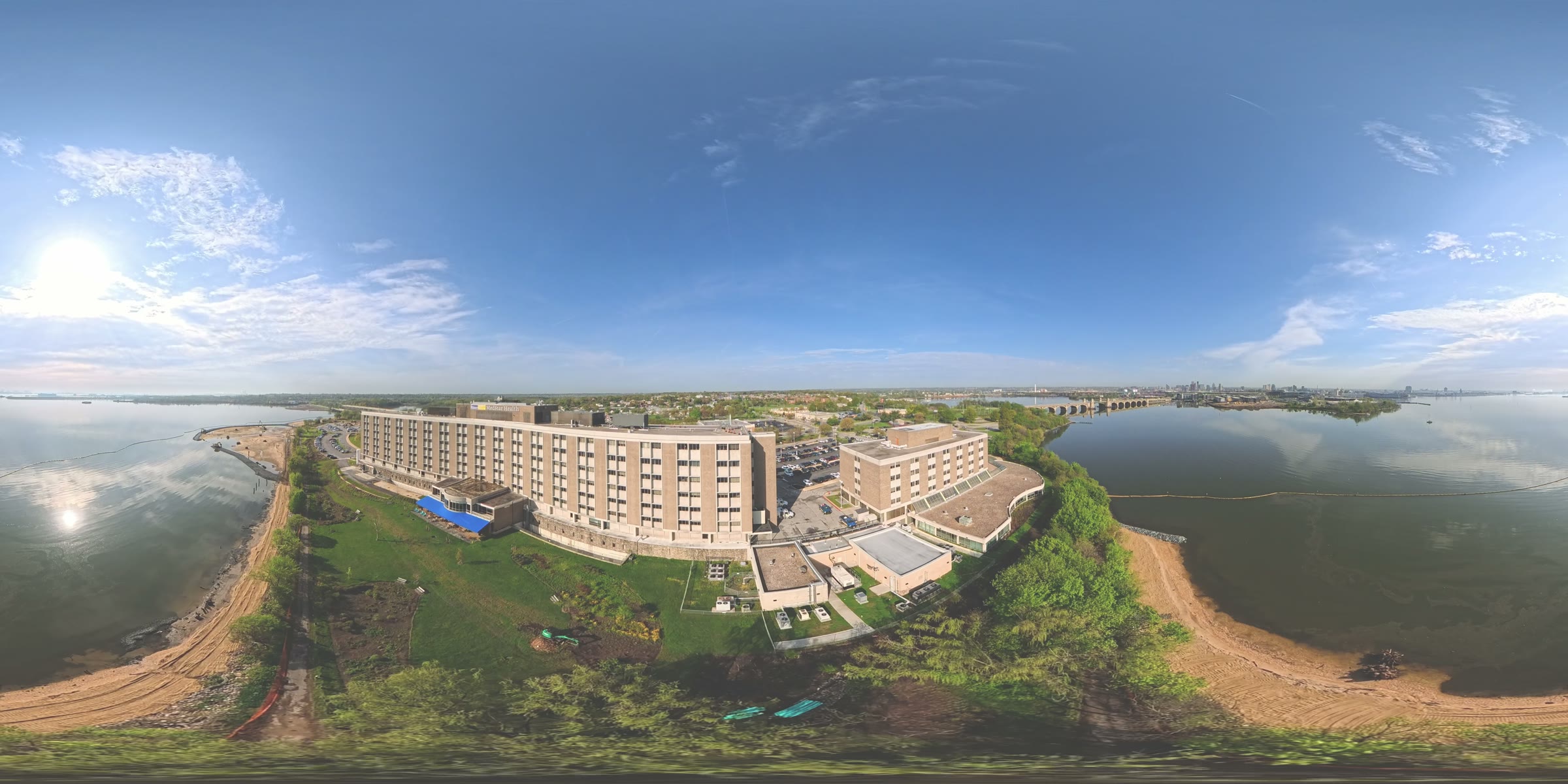 Full 360-degree aerial view of the Parexel waterfront campus, showing the main building, shoreline, and a distant bridge and skyline.