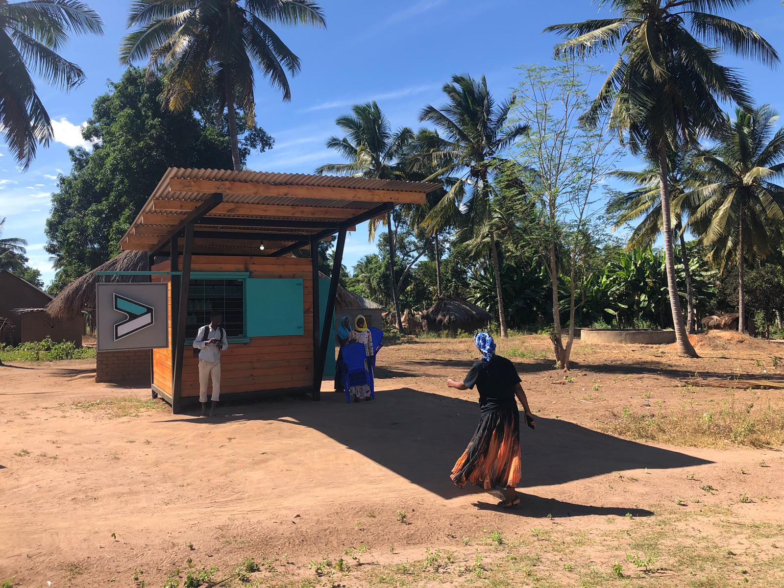 Woman walking towards a Jaza Energy hub which has two people standing in front of it.