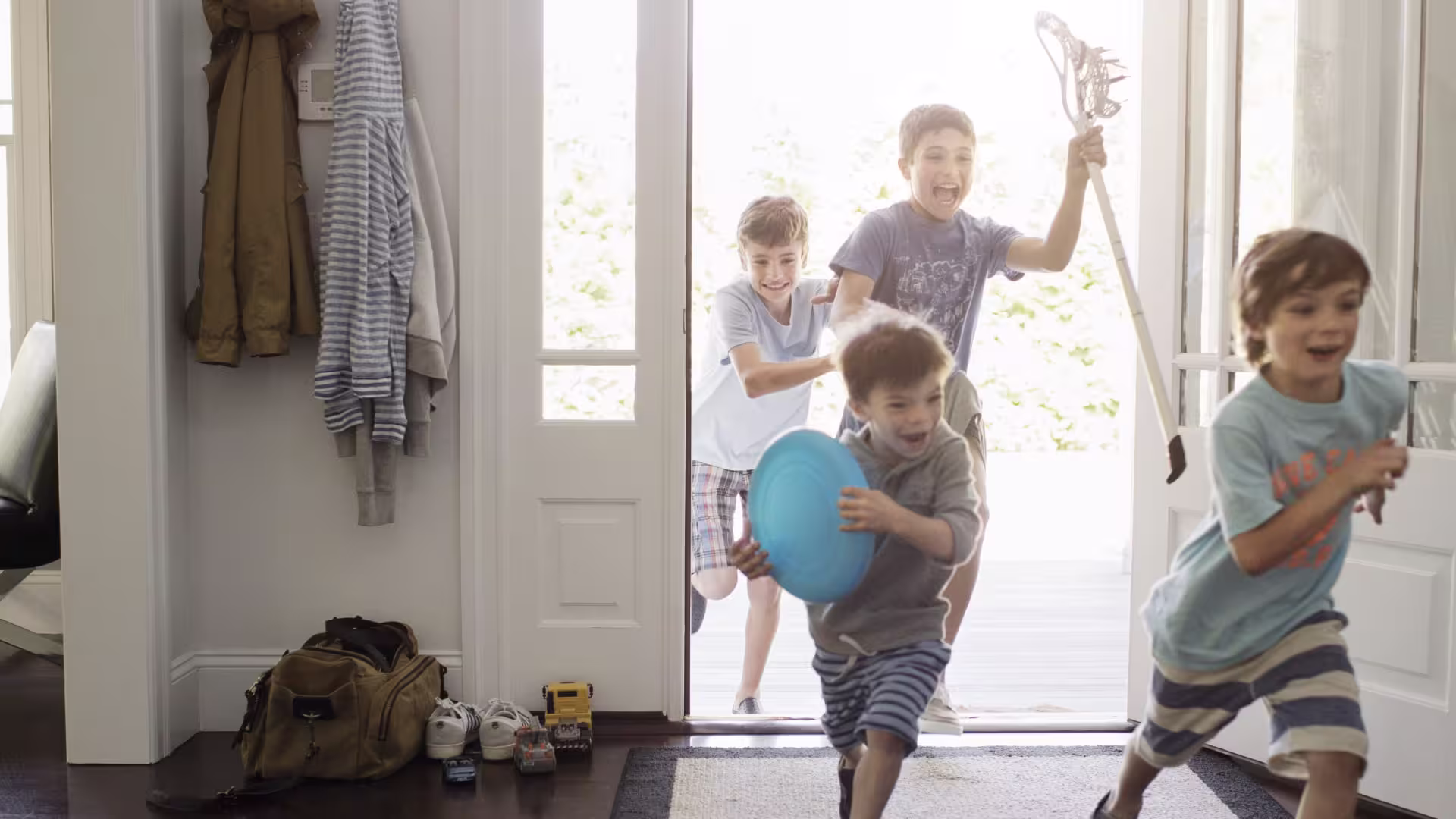 For young boys holding toys and running through the open front door of a home