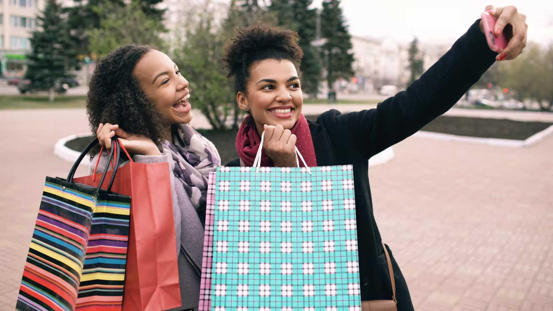 Two women holding colorful shopping bags, posing for a selfie photo
