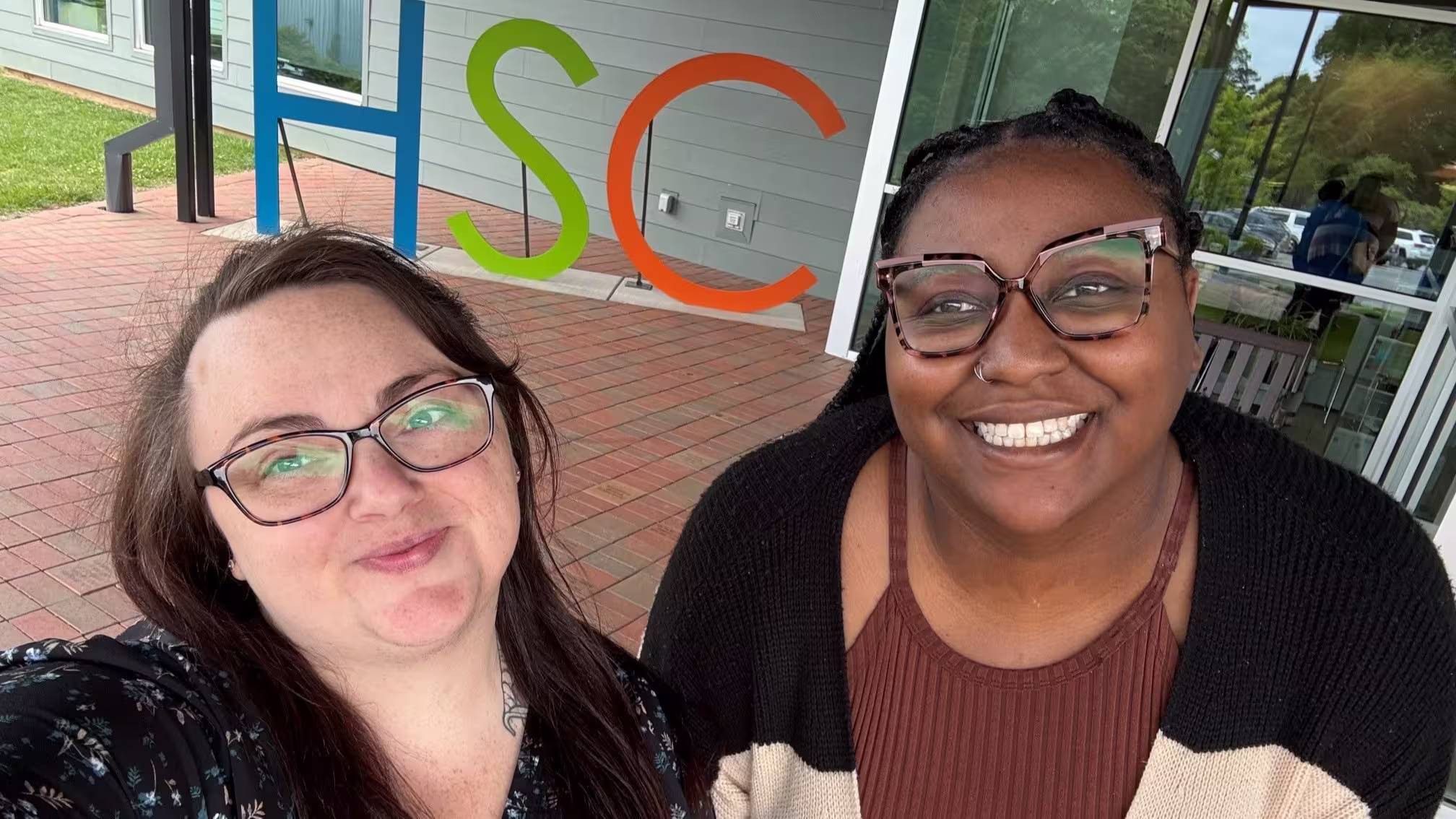 A selfie of two team members standing in front of an HSC sign