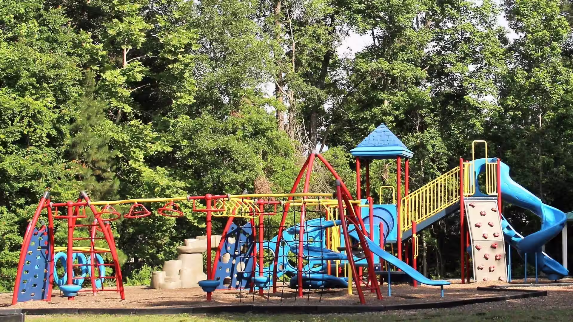 Red, yellow and blue playground with a slide, rock wall, jungle gym and castle tower.